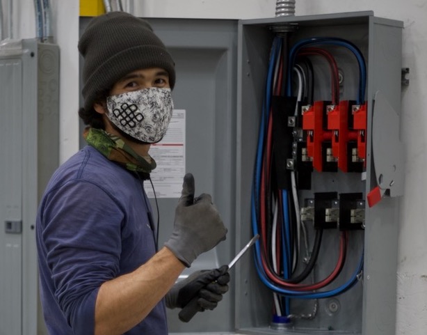 An OHM Electrician gives a "thumbs up" near a panel box.