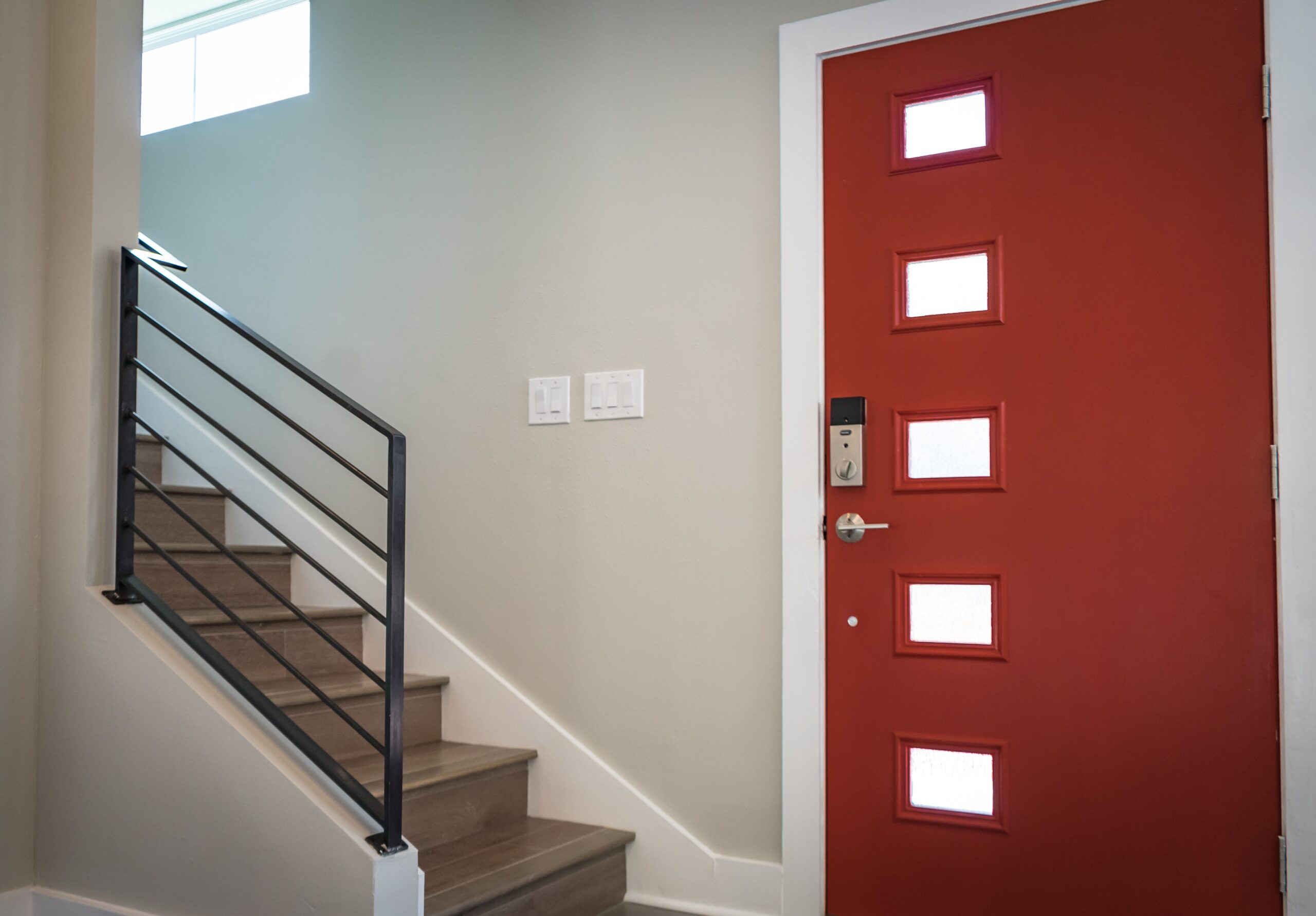 An entryway in a home features a bold red door and a stairway to the left.